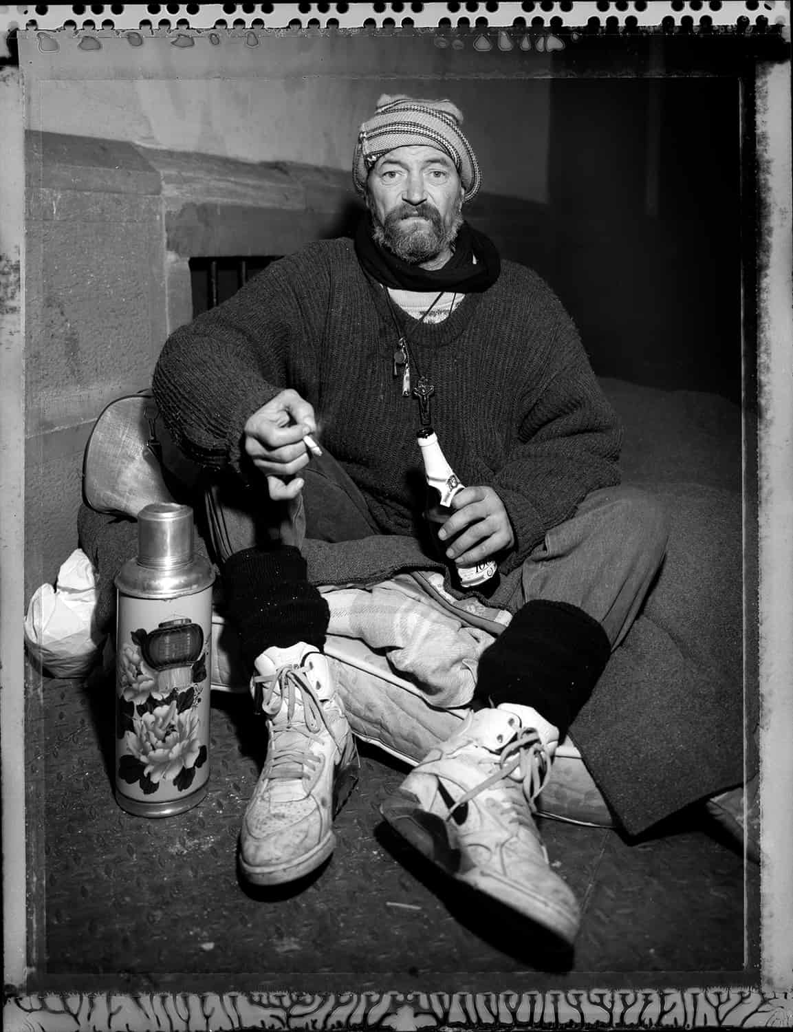 photo noir et blanc d'un sans domicile fixe assis sur un couchage dans la rue © francois nussbaumer