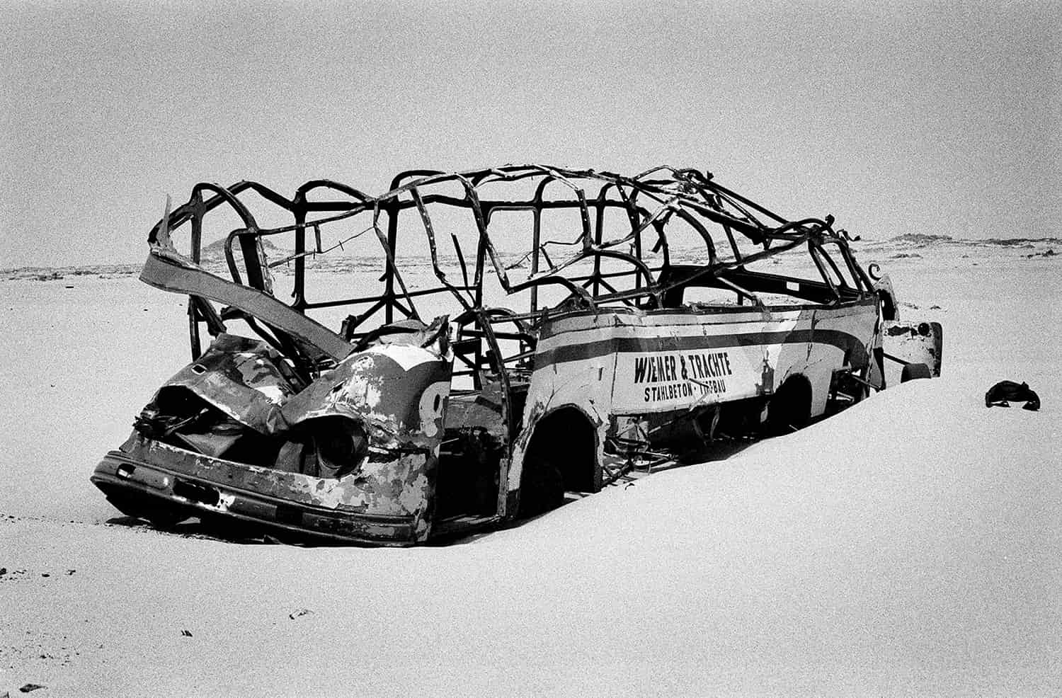 photographie noir et blanc d'une carcasse d'un bus portant l'inscription Wiemer & Trachte dans le désert © francois nussbaumer
