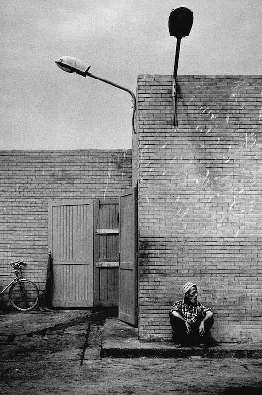 photographie noir et blanc d'un homme portant une casquette de pière musulmane assis devant un mur de brique © francois nussbaumer