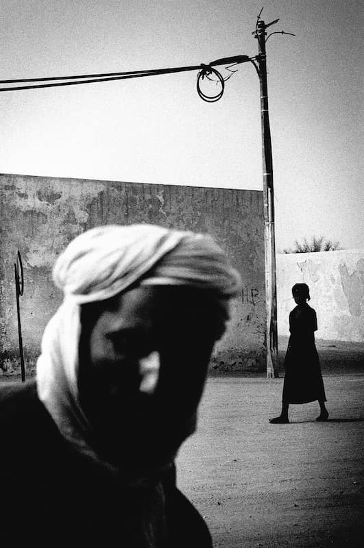 photographie noir et blanc d'un homme avec un turban en premier plan et une enfant passant en arrière plan © francois nussbaumer